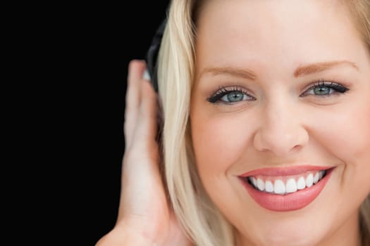 Blonde woman closing her eyes while listening to music against a black background