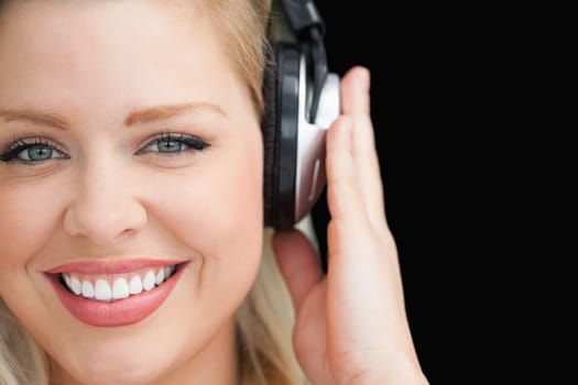 Smiling blonde woman listening to music through headphones against a black background