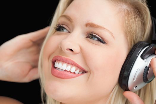 Happy blonde woman listening to music through headphones against a black background