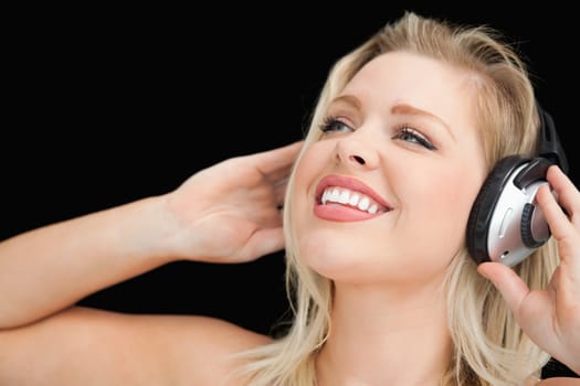 Cheerful blonde woman wearing headphones against a black background