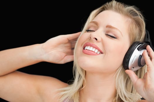 Joyful blonde woman listening to music through headphones against a black background