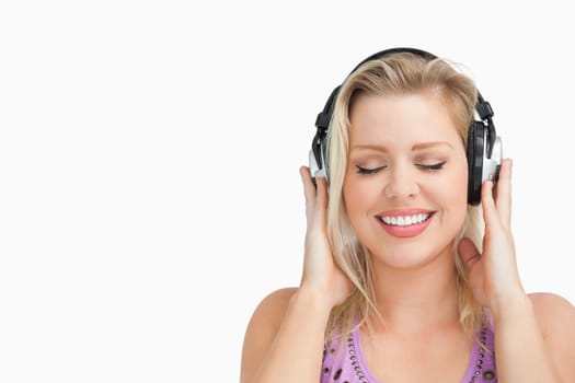 Happy blonde woman listening to music with headphones against a white background