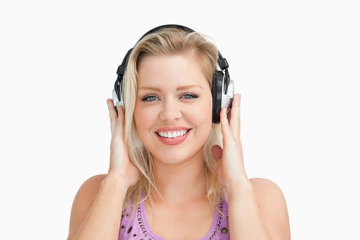 Smiling blonde woman placing her hands on her headphones against a white background