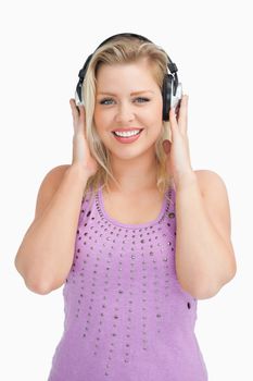 Happy blonde woman placing her hands on her headphones against a white background