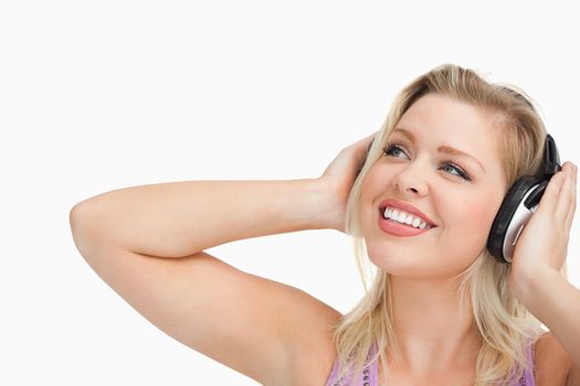 Smiling blonde woman looking up while listening to music against a white background