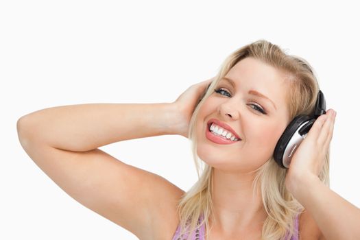 Blonde woman raising her arms while listening to music against a white background