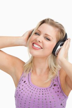 Smiling blonde woman wearing headphones while touching them against a white background
