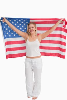 Cheerful blonde woman raising the American flag against a white background