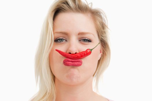 Blonde woman placing a chili between her nose and her mouth against a white background