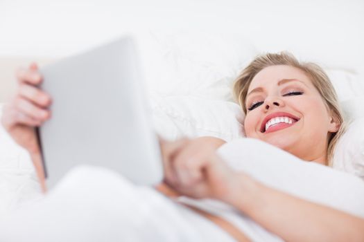 Young woman holding an ebook while lying on a bed