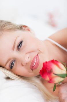 Blue eyed woman with a rose in a bed