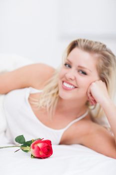 Young woman with a rose smiling on her bed