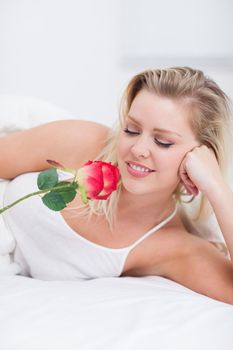 Young woman looking at her pink rose while lying on her bed