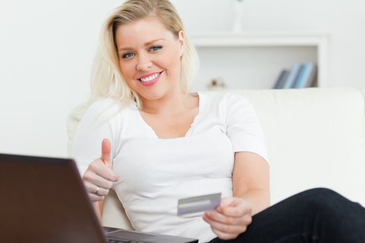 Woman with a credit and using a laptop on a sofa