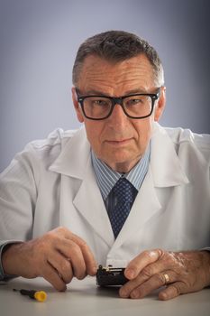 An older male wearing a white lab coat and reaparing electronic equipments, like a technician or a repair man.