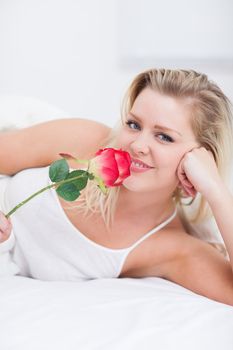 Young woman smelling a pink rose on her bed