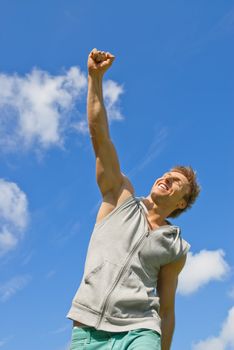 Smiling young man with his arm raised in joy, outdoors on a sunny day.