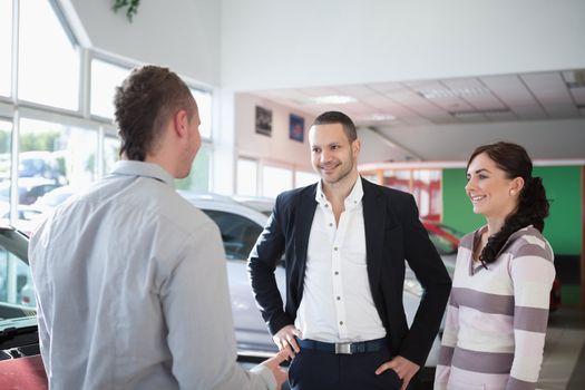 Car dealer chatting with a couple in a car shop
