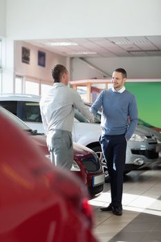 Salesman shaking hand to a customer in a car shop