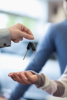 Salesman holding keys over the hand of a customer in a carshop