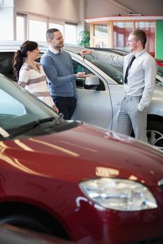 Smiling salesman giving keys to a happy couple in a car shop