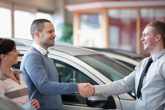 Smiling salesman shaking a customer hand in a car shop