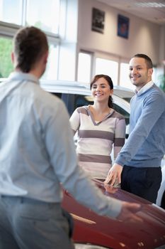 Couple smiling and chatting with a salesman in a carshop