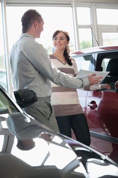 Salesman showing documents ta a woman in a car shop