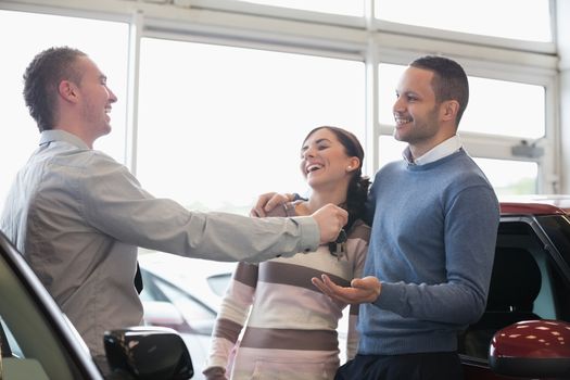Laughing couple receiving keys from a salesman in a car shop