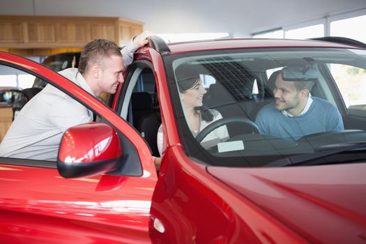 Couple listening to a salesman while sitting on a car in a car shop