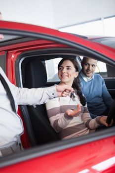 Smiling woman receiving keys from a salesman while sitting in a car