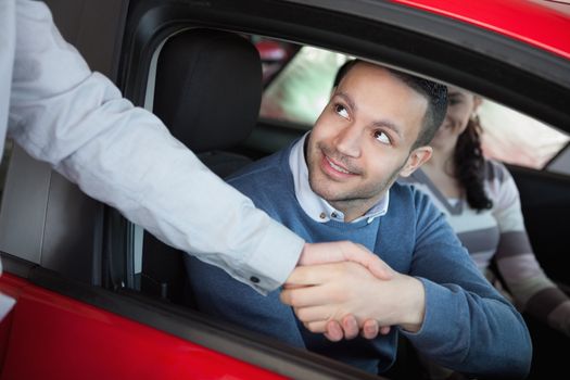 Man shaking the hand of a car dealer while sitting on a car