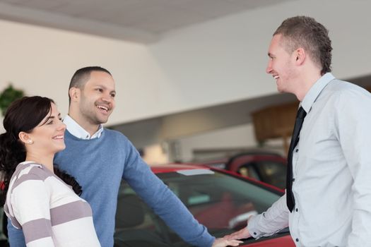 Laughing couple talking with a salesman in a car shop