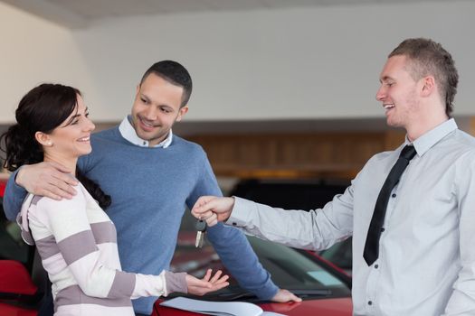 Couple embracing while receiving keys from a salesman in a car shop