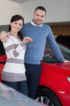 Happy couple embracing while holding keys in a car shop