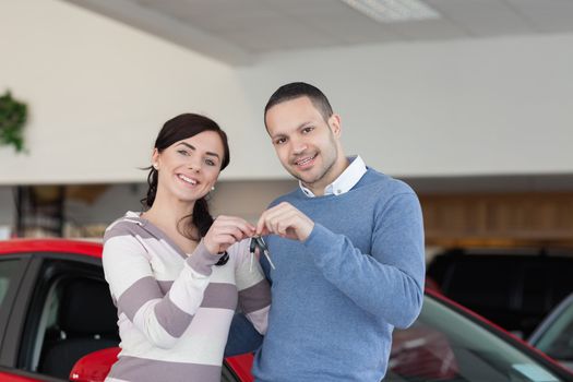 Smiling couple standing next to a car while holding keys