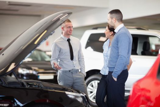 Couple standing in front of an open car engine in a car shop
