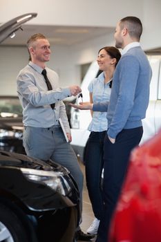 Salesman giving car keys to a couple in front of an open car engine