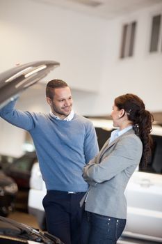 Smiling couple in front of an open car engine in a car shop