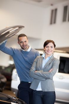 Happy couple in front of an open engine in a car shop