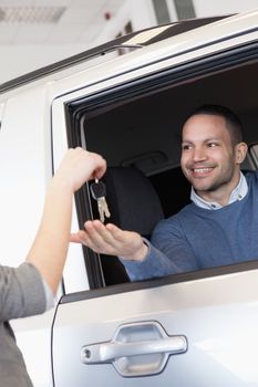 Smiling man in a car receiving a car key in a car shop