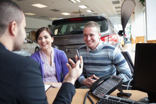Couple smiling while talking with a salesman in a car shop