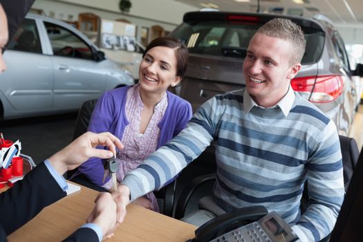 Happy couple shaking the hand of a salesman while receiving car keys