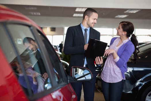Salesman talking to a smiling woman next to a car in a car shop