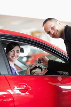 Happy salesman giving car keys to a woman in a car shop