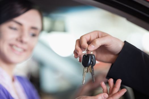 Woman in a car receiving keys from a car dealer