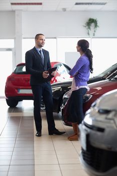 Salesman and a woman talking next to a car in a car shop