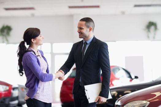 Smiling salesman shaking the hand of a woman in a car shop