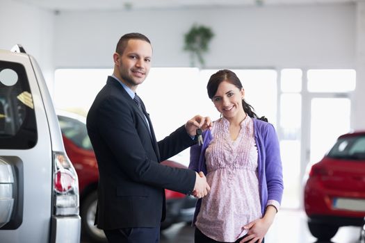 Salesman shaking hand and giving keys to a woman in a car shop