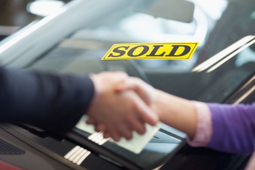 People shaking hands in front of a sold car